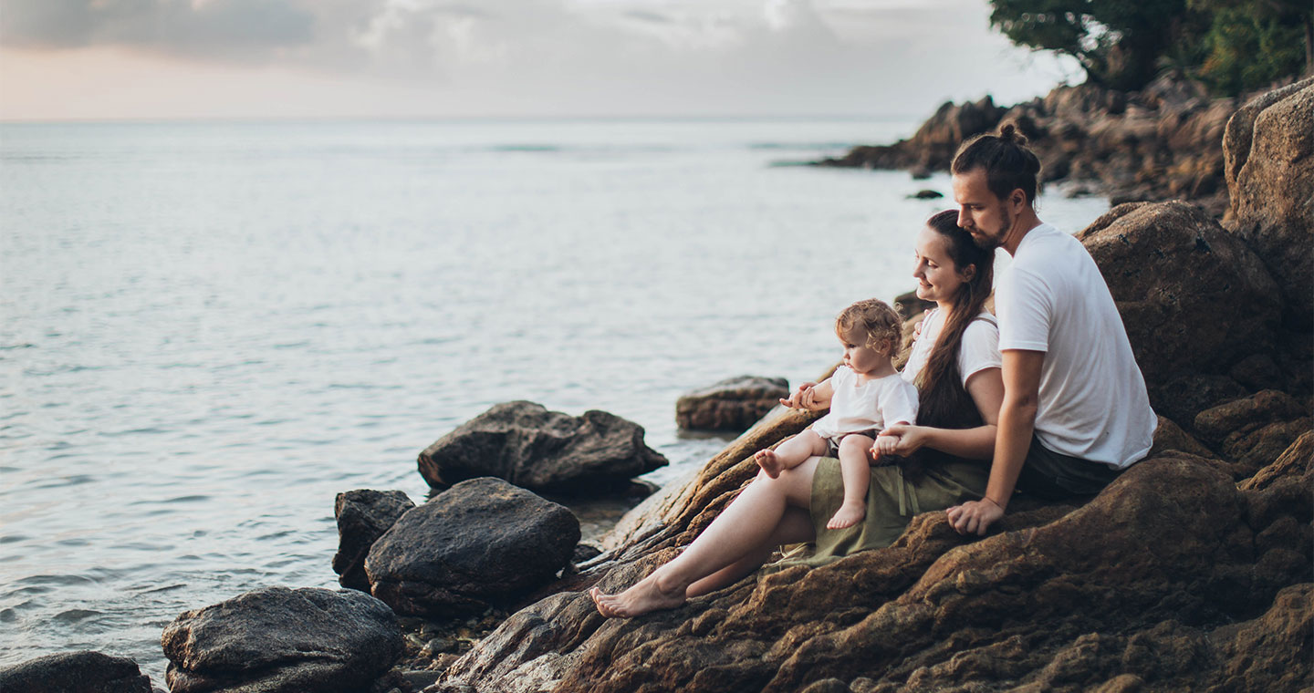 Hawaii family guide for your family getaway - a family of three sitting on the rocks by the beach