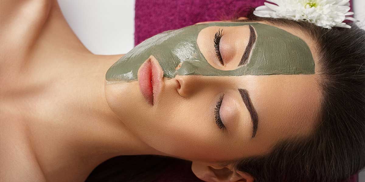 Woman with clay facial mask in beauty spa with her hawaii massage
